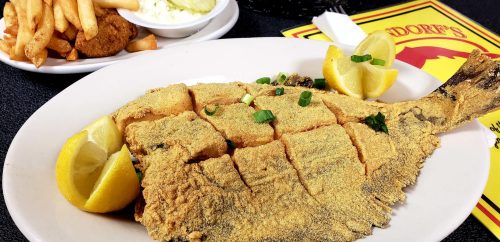 A plate of fried fish garnished with lemon and green onions, served with fries and a side of coleslaw.
