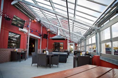 A spacious, modern outdoor dining area with a glass roof, featuring wicker furniture and a cozy atmosphere.