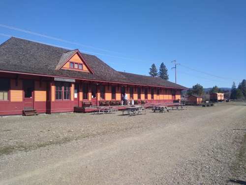 Historic train station with colorful wooden exterior, picnic tables outside, and a clear blue sky.