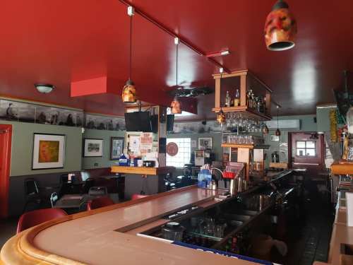 Interior of a bar with a red ceiling, wooden counter, hanging lights, and seating area. Decor includes framed photos.