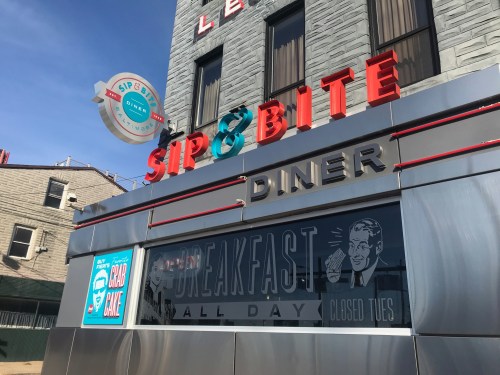 Exterior of Sip & Bite Diner with a bright sign, featuring "Breakfast All Day" and "Closed Tues" on the window.