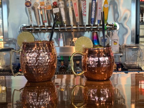 Two copper mugs filled with drinks, garnished with lime slices, sit on a bar counter with taps in the background.