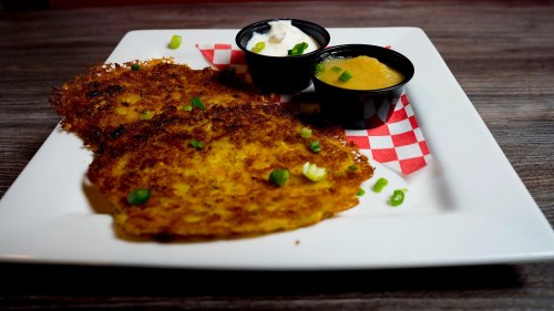 Two crispy potato pancakes on a plate, garnished with green onions, served with sour cream and applesauce in small cups.