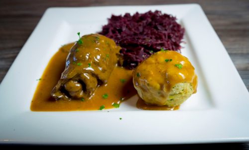 A plate featuring stuffed cabbage roll in sauce, a scoop of savory dumpling, and a side of red cabbage.