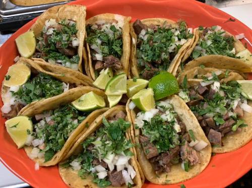 A vibrant platter of tacos filled with meat, topped with onions, cilantro, and lime wedges.