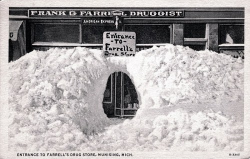 A snowy scene with a sign reading "Entrance to Farrell's Drug Store" in front of a drugstore in Munising, Michigan.