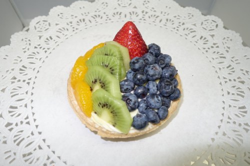 A fruit tart topped with strawberries, blueberries, kiwi, and mandarin oranges on a decorative lace doily.