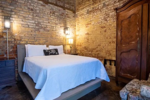 Cozy bedroom with a brick wall, a queen bed, bedside lamps, and a vintage wardrobe.