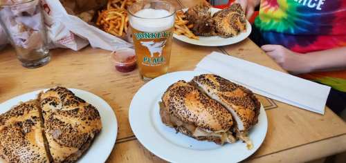 A table with poppy seed bagels filled with meat, fries, and a glass of beer, set in a casual dining environment.