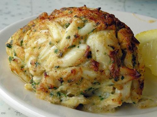 A golden-brown crab cake served on a plate with a lemon wedge, showcasing its flaky texture and herbs.