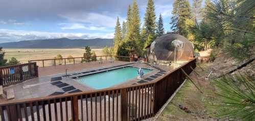 A serene outdoor pool area surrounded by trees, with a dome structure nearby and mountains in the background.