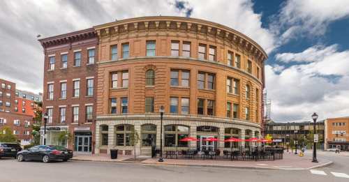 Historic brick building with large windows, featuring outdoor seating and a cloudy sky in the background.
