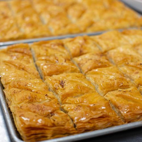 A tray of golden-brown baklava, cut into rectangular pieces, showcasing its flaky layers and syrupy glaze.