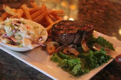 A plate featuring a grilled steak, sautéed mushrooms, coleslaw, and crispy French fries on a marble table.
