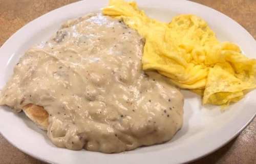A plate featuring a biscuit smothered in creamy sausage gravy alongside a fluffy yellow omelet.