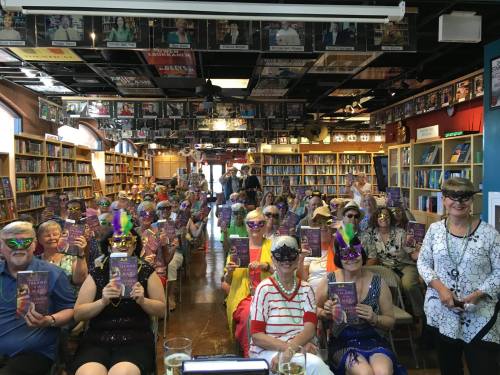 A large group of seniors in colorful hats and masks, holding books, gathered in a bookstore for an event.