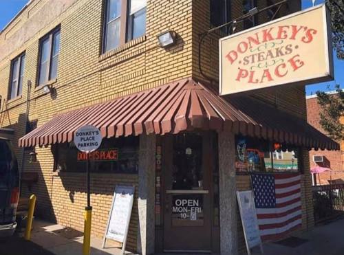 Exterior of Donkey's Place, a steakhouse with a red awning, sign, and American flag displayed. Open Monday to Friday.