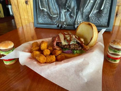 A juicy burger with cheese and toppings, served with crispy tater tots, on a wooden table with decorative mini burgers.