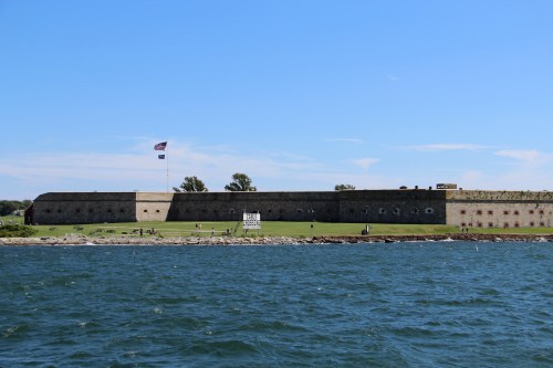 A historic fort with a flag, surrounded by water and grassy areas, under a clear blue sky.