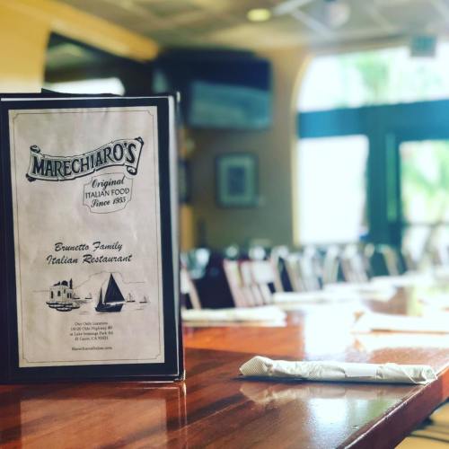 A menu from Marechiaro's Italian Restaurant on a wooden table, with empty chairs and a bright, inviting atmosphere.