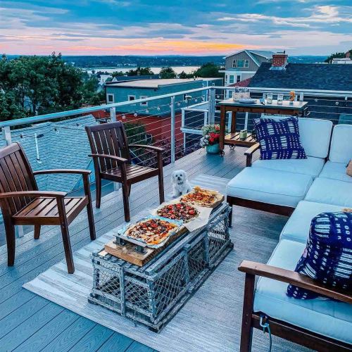 A cozy outdoor patio with wooden furniture, a platter of food, and a dog, overlooking a scenic sunset view.