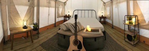 Cozy glamping tent interior with a bed, guitar, lanterns, and plants, creating a warm, inviting atmosphere.