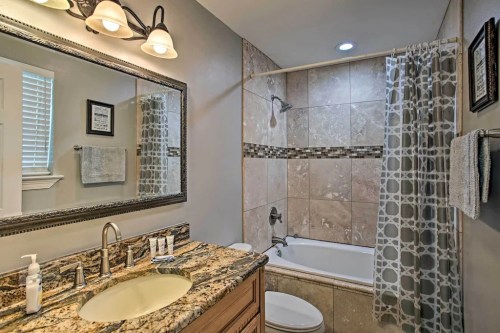 A modern bathroom featuring a bathtub, shower, granite countertop, and decorative tile accents.