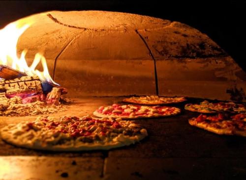 Pizzas baking in a wood-fired oven with flames and glowing embers in the background.