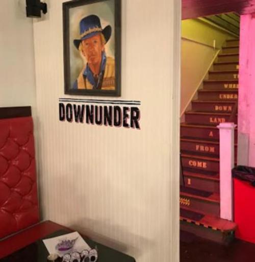 A wall with a portrait of a man in a cowboy hat and the word "DOWNUNDER" above a staircase with colorful lighting.