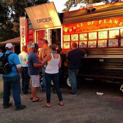 A food truck with a menu displayed, customers lining up to order, and a warm sunset in the background.