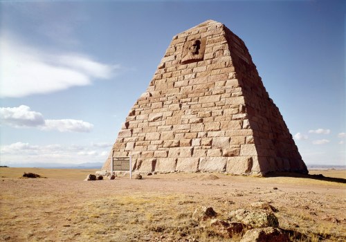 A large stone pyramid structure stands on a barren landscape under a blue sky with scattered clouds.