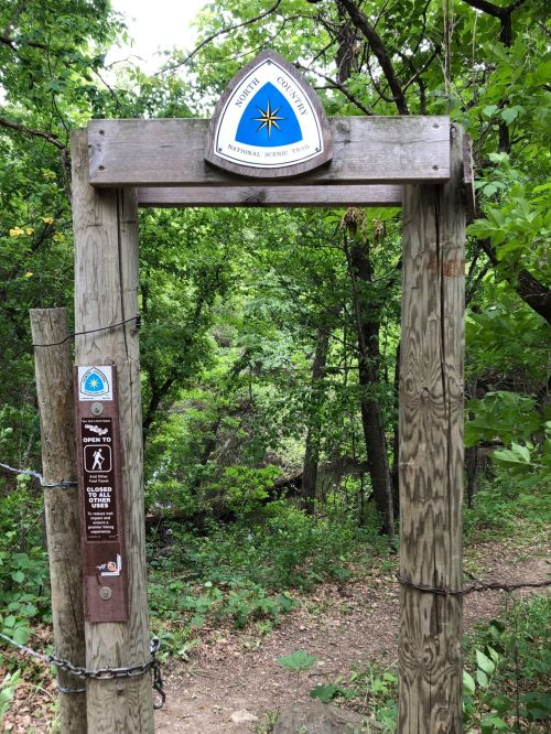 Wooden archway marking the entrance to a nature trail, surrounded by lush green trees.