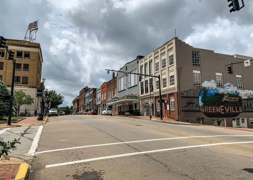 A quiet street in Greenville with historic buildings, traffic lights, and a cloudy sky overhead.