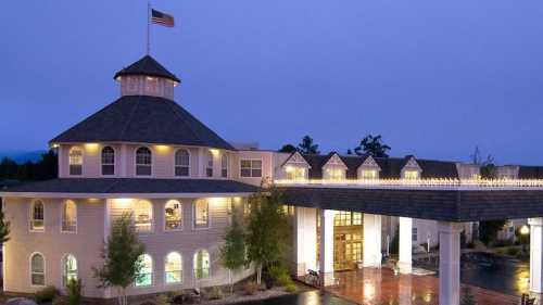 A well-lit, round building with a flag on top, featuring a welcoming entrance and surrounded by trees at dusk.