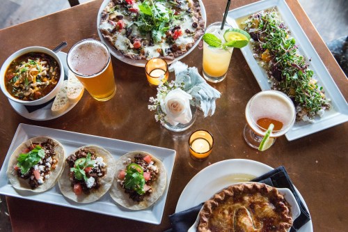 A vibrant spread of tacos, a pie, drinks, and appetizers on a table, surrounded by candles and flowers.
