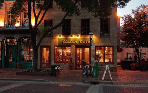 Aster Cafe illuminated at night, featuring warm lights and outdoor seating in a charming brick setting.