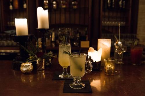 Two cocktails on a bar with candles and decorative lights, creating a warm, inviting atmosphere.