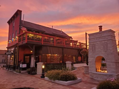 A charming restaurant with a wooden deck, surrounded by colorful sunset skies and decorative outdoor lighting.