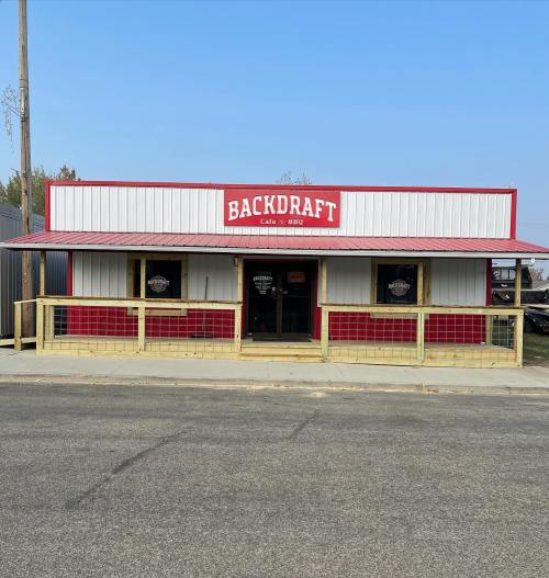 Exterior of "Backdraft Cafe & BBQ," a red and white building with a wooden railing and clear blue sky.