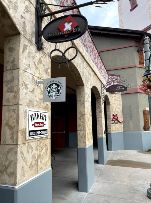 A bakery storefront with signs for baked goods and a Starbucks, featuring decorative arches and a charming exterior.
