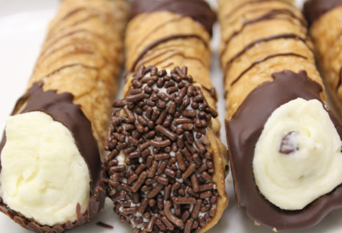 Three chocolate-dipped cannoli filled with cream, one topped with chocolate sprinkles.