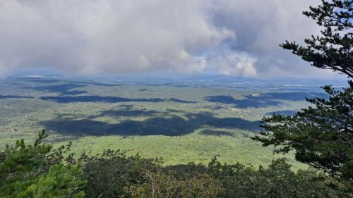 A panoramic view of lush green hills under a cloudy sky, with shadows cast across the landscape.