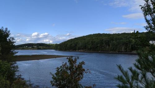 A serene lake surrounded by lush green hills under a partly cloudy blue sky.