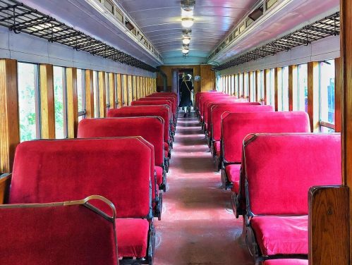 Interior of a vintage train car featuring rows of red upholstered seats and wooden paneling.
