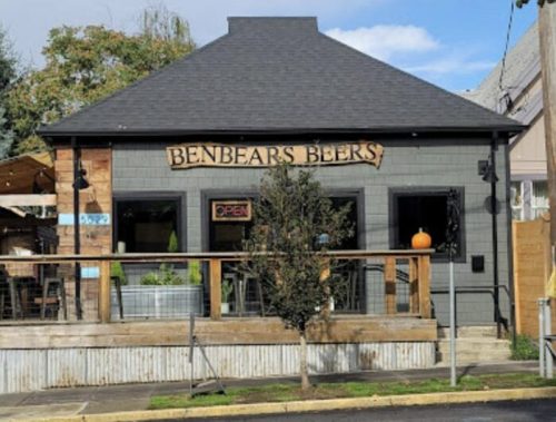 A cozy pub named "Benbear's Beers" with outdoor seating and an open sign, set against a clear blue sky.