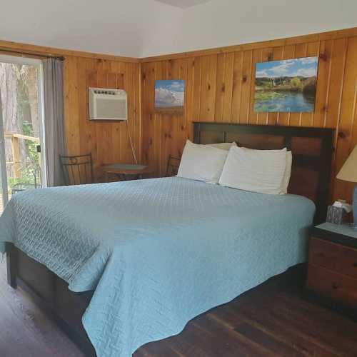 Cozy bedroom with wooden walls, a blue quilted bedspread, and nature-themed artwork on the walls.