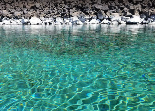 Clear turquoise water gently rippling over a rocky shoreline, reflecting light and creating a serene atmosphere.