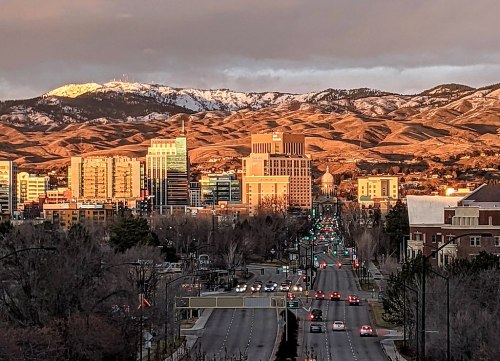 A city skyline at sunset, with mountains in the background and a road lined with traffic lights.
