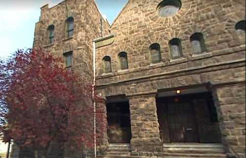 Historic stone building with large arched windows and a red tree in front, showcasing a classic architectural style.