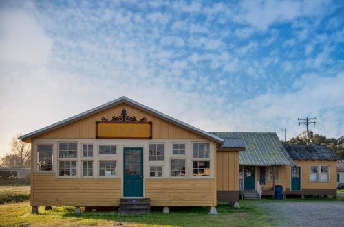 A charming yellow antique shop with large windows, set against a blue sky and grassy landscape.